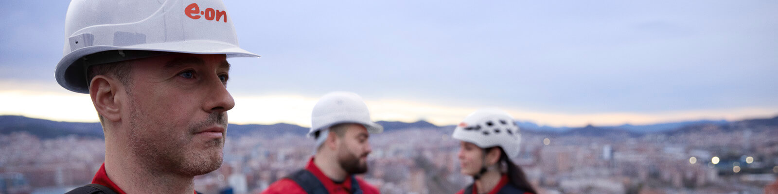 A worker in an E.ON branded hard hat, with two other workers seen chatting in the background